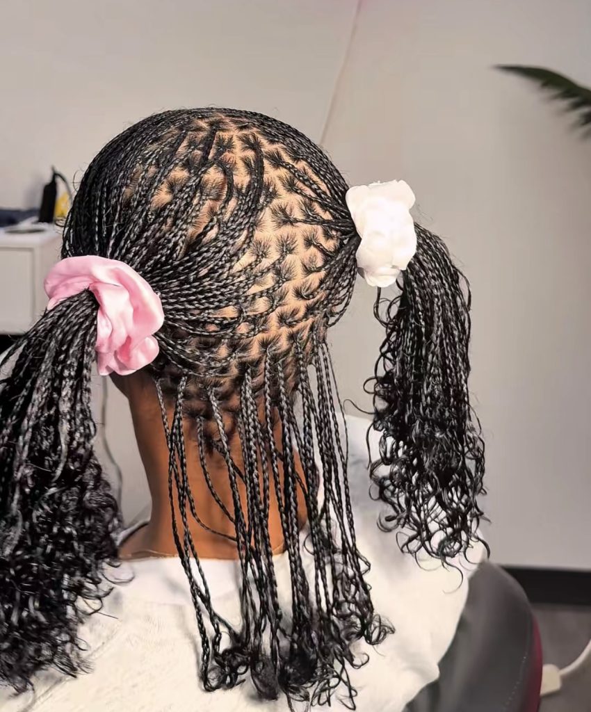mini braids on natural hair with curly ends styled in two messy ponytails with scrunchies